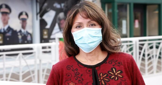 Attractive woman with long dark hair wearing a covid mask for coronavirus epidemic turns head and looks into camera. Hand-held medium shot of olde asian model.