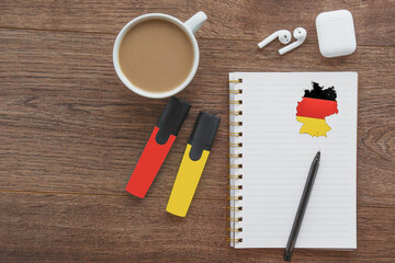notepad with flag of German, wireless headphones, coffee cup, pen, markers on brown table, study...