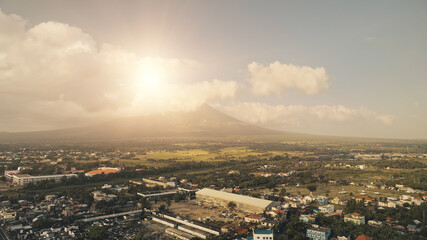 Sun shine over Mayon volcano erupt at Legazpi cityscape aerial. Epic Philippines landmark at urban buildings and roads. Green grass valley of mount hillside. Cinematic nature and tropic town