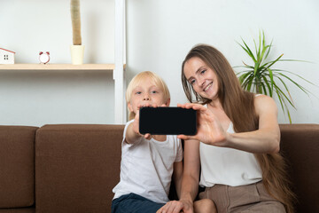 Young mom takes selfie with her son. Mom and child show screen of smartphone