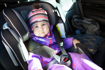 Baby sitting in a child safety seat in forward-facing position on the back car chair, adjustable headrest