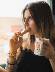 Mujer atractiva tomando un cafe y una barrita energética mientras descansa en el trabajo. Mirando por la ventana a traves del cristal en un dia soleado.