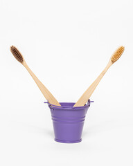 Small purple bucket with bamboo toothbrushes on white background