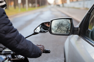 Motorcycle rider touching side mirror of a car when riding nearby on a road, close up view