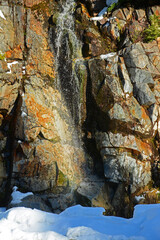 Small waterfall on golden brown rock cliff in winter