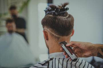 detail of a young man with tattooed arms cuts a man's hair in a barber shop