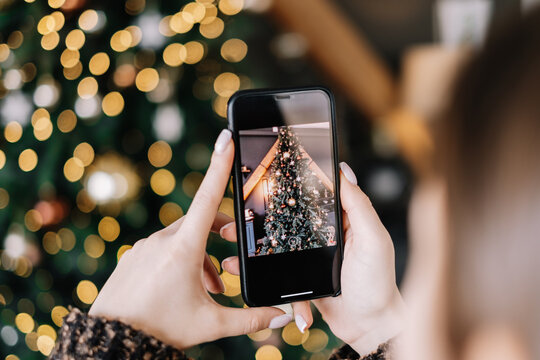 Young woman takes pictures of Christmas tree on smartphone. Close-up