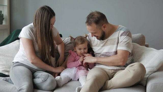 Parenthood. Young parents playing with their cute little daughter on sofa. Young carefree parents and child laugh play cuddling at home enjoy funny game on couch. Young family of three. Mum and dad 