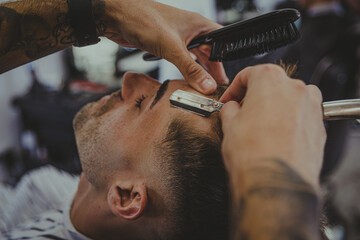 detail of a young man with tattooed arms cuts a man's hair in a barber shop