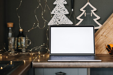 Laptop computer with white blank screen mock up, on the kitchen table with Christmas decoration.