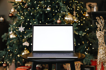 Laptop computer with white blank screen mock up, on the table near Christmas tree.