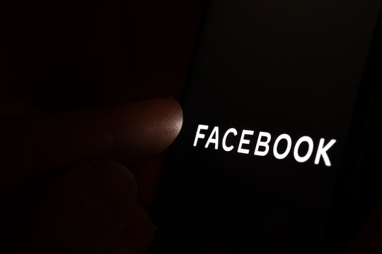 New Facebook company logo on the dark screen and finger about to touch it. Conceptual photo.