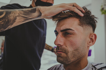 Obraz premium a young man with tattooed arms cuts a man's hair in a barbershop