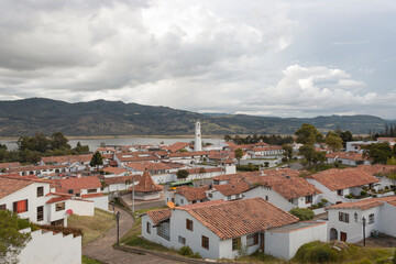 Guatavita colombian town cityscape with white structure, red ceramic roofs and andean mountains and tominé lake at background at evening. 