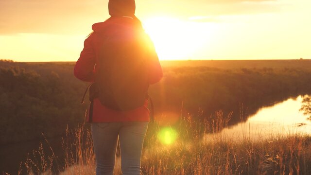 Girl Traveler In The Rays Of The Sunset Sun With A Backpack. Young Woman Tourist Walks On A High Mountain Meeting The Sunrise. Thirst For Adventure In Finding Yourself. Research Findings Of Various