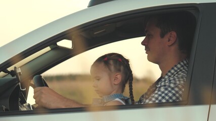 Dad teaches his little daughter to turn steering wheel while sitting in his car in drivers seat. father travels with children by car. driver and kid are driving. happy family and childhood concept