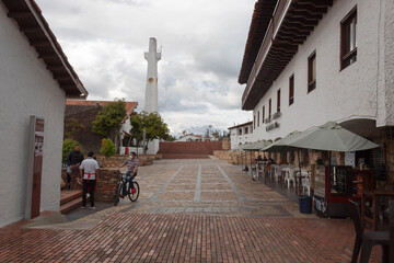 GUATAVITA, COLOMBIA - Guatavita main square alley entrance with chairs and umbrellas and clock tower at background. 