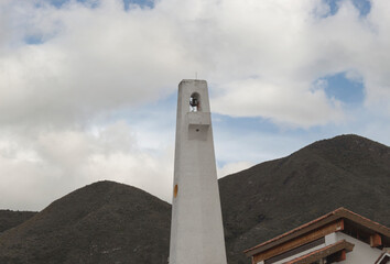 Obraz premium GUATAVITA, COLOMBIA - Bell and clock white tower with green mountains and white clouds at background