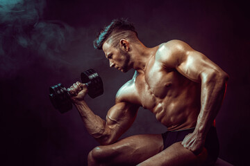 Athletic man flexing muscles in studio on dark background with smoke. Strong bodybuilder with...