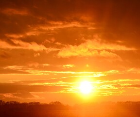 Fototapeta premium Сфотографирован закат с оранжевыми облаками и ярким белым солнцем