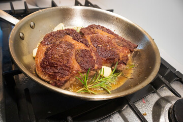 Ribeye beef steak in a stainless steel pan with butter.