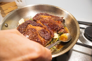 Ribeye beef steak in a stainless steel pan with butter.