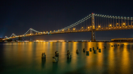 Night image of the Oakland Bridge as it leaves San Francisco and heads northwest into Oakland with lighted reflections of sunken pier ballasts