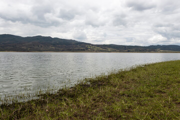 Guatavita Lake grass shore with sky water reflection and mountains
