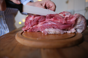 woman at home in the kitchen cuts an appetizing piece of poultry meat into slices with a porcelain knife, raw turkey drumstick, concept of cooking homemade food