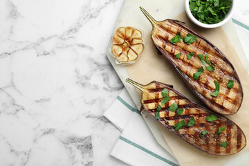 Delicious grilled eggplant halves with parsley on white marble table, flat lay. Space for text