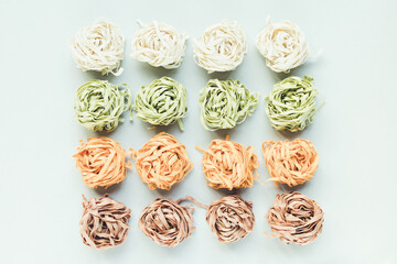 Raw traditional Italian tagliatelle pasta noodles nests of a different color - spinach, potato, carrot, amaranth, light background. Natural food coloring from Vegetables concept. Close up, copy space