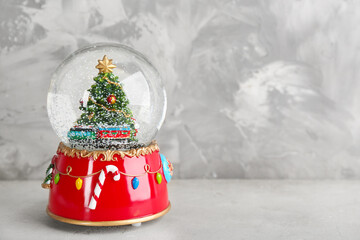 Beautiful snow globe with Christmas tree on light grey stone table. Space for text