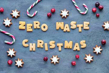 Text Zero Waste Christmas made from cookies. Xmas top view. Minimal design with candy canes, star cookies and fresh cranberry, Natural Christmas decorations on grey textured aged sbackground.