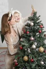 Mother helping to her little girl to put a star topper on the Christmas tree. Joy of family winter holidays at home.