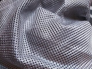 Synthetic polyester fabric with holes. Abstract background. A wave-folded piece of fabric in gray or silver color.