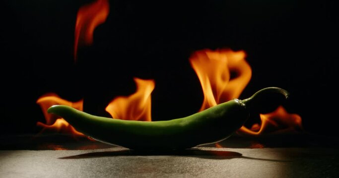 Hot green pepper set on flames. Epic cinematic shot of chili pepper burning in fire - art food concept close up shot 4k footage