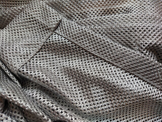 Synthetic polyester fabric with holes. Abstract background. A wave-folded piece of fabric in gray or silver color. Neatly hemmed fabric.