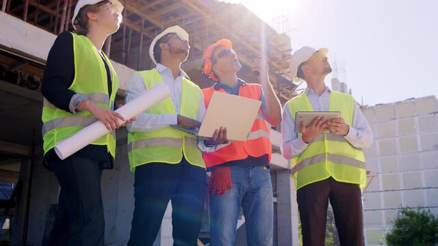 Full equipment team multiethnic of construction in the middle of construction site using the ration to have a conversation with other construction workers from the roof top