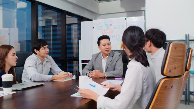 Group of happy Asian business people discuss together in team brainstorm meeting and clap hand, work late night in office. Corporate business, coworker teamwork, or project success celebration concept
