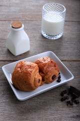 Fresh Baked Chocolate Croissants (Pain au Chocolat) with Milk for Breakfast. Served on White Plate on Rustic Table Copy Space for Text