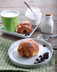 Fresh Baked Chocolate Croissants (Pain au Chocolat) with Milk for Breakfast. Served on White Plate on Rustic Table Copy Space for Text