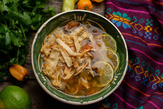 Mexican lime soup with chicken on wooden background