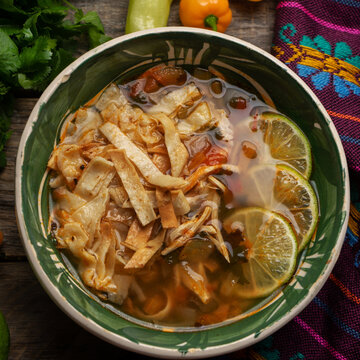 Mexican lime soup with chicken on wooden background