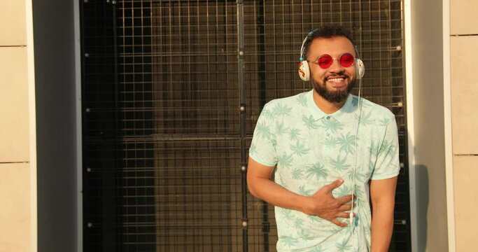 The happy african man in sunglasses and headphones is laughing outdoor. 4k footage.