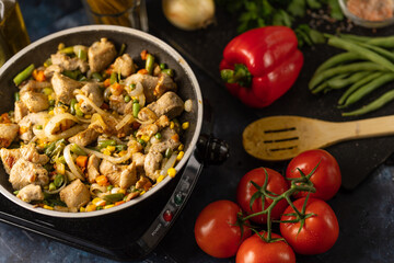Pan with frying meat and mix of vegetables on marble dark blue table with variety of ingredients background. Backstage of cooking pasta. Concept of cooking process. View from above. Tasty recipe.
