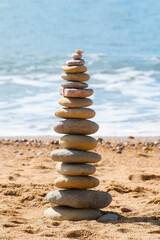Fototapeta na wymiar Stacked zen stones on sandy beach with quiet sea waters in background.