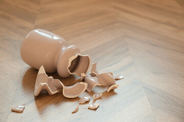 Broken pink ceramic vase on wooden floor. Space for text