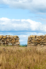 Hills with a green lush grass, fields and meadows against blue cloudy sky with a stone walls.