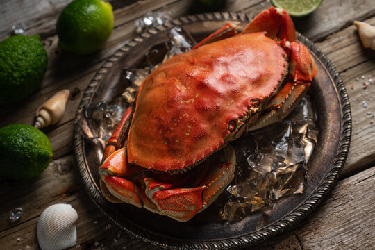 Tasty cooked crab on black round plate with ice cubes served with lime and seashells on rustic wooden background. Delicious meal. Seafood concept. View from above.