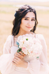 Portrait of the bride in a powdery dress with a wedding bouquet in her hands on the background of nature